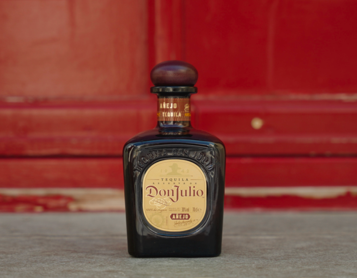 Botella de tequila Don Julio Añejo frente a una puerta roja.