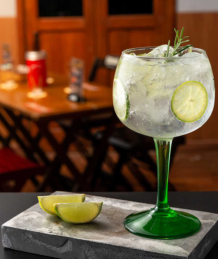 A Tanqueray gin balloon glass filled with ice and garnished with lime and herbs.