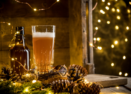 Bottle and glass of beer, surrounded by pine cones and fairy lights
