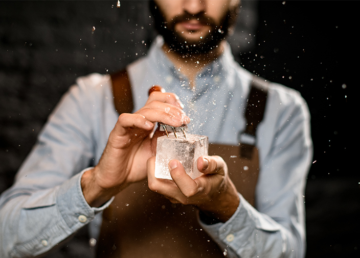 El bartender sostiene un cubo de hielo cúbico perfecto y usa una herramienta profesional de tres puntas para perfeccionar la forma.
