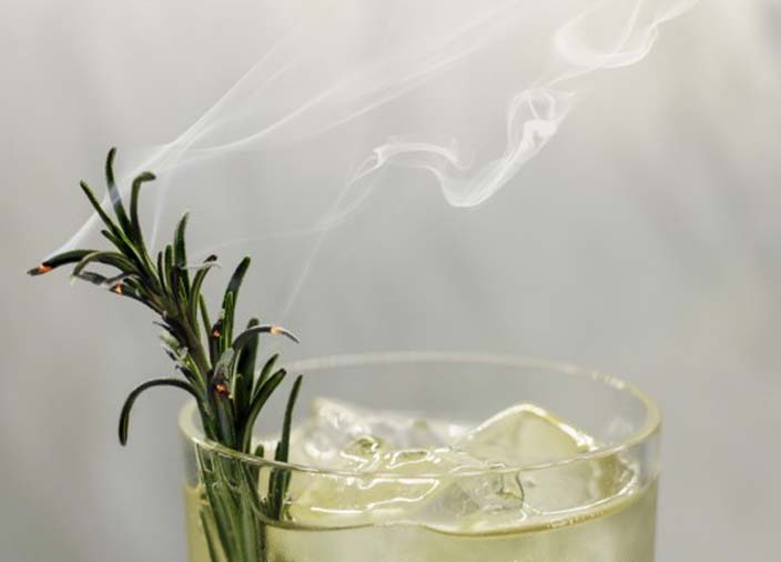 Close-up view of the rim of a cocktail glass with a smoked herb/garnish in it.
