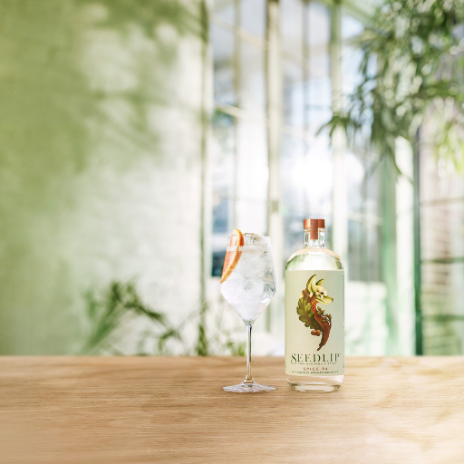 Bottle of Seedlip Spice 94 on table beside cocktail