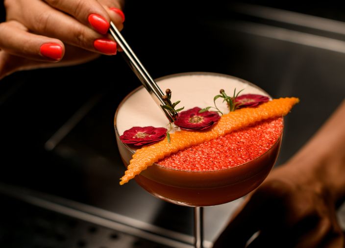 Female bartender adding garnish to a serve using tongs.