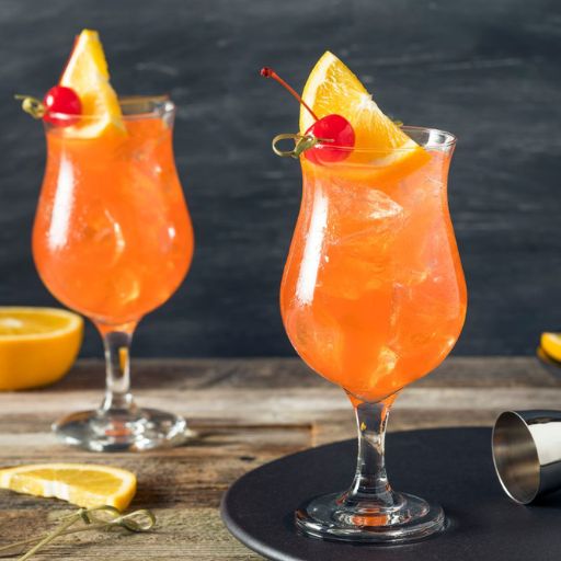 Two Singapore Slings surrounded by orange slices and garnished with an orange wedge and cherry 