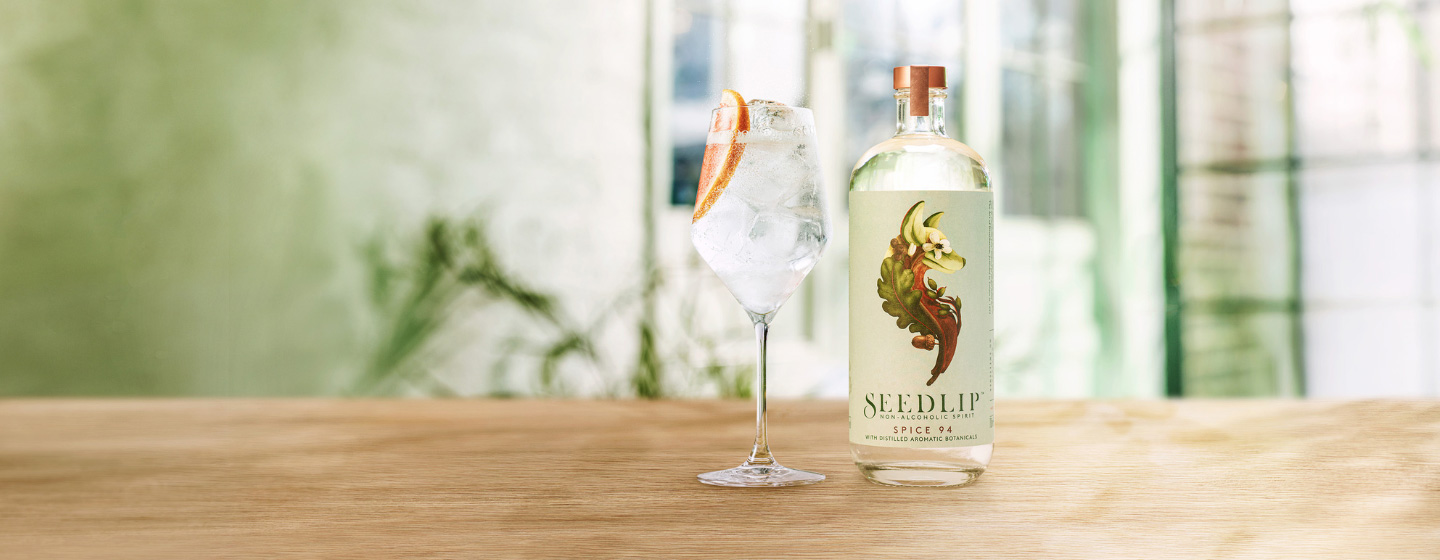 Bottle of Seedlip Spice 94 on table beside cocktail 