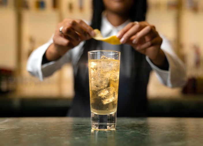 Bartender twisting lemon peel above highball