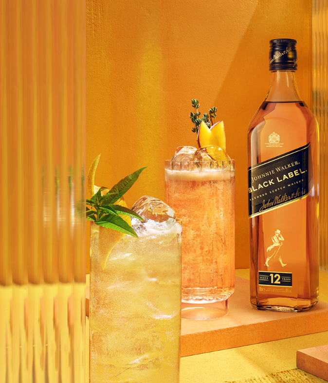 Johnnie Walker Lemon Highball served in a Highball glass with garnish & bottle of Johnnie Walker Black Label 