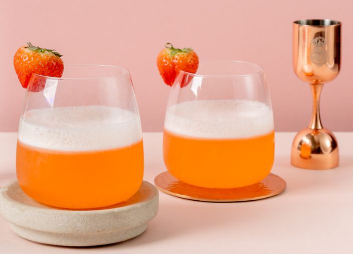 Two seedlip cocktails garnished with strawberries beside a jigger 