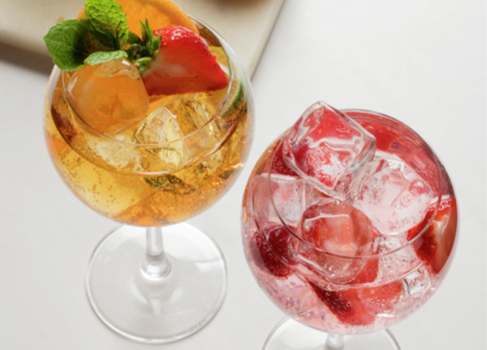 Dos coloridos cócteles en copas de ginebra con hielo y decoraciones de frutas