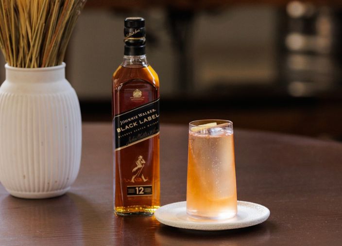 Cóctel color naranja con hielo acompañado de una botella de licor.