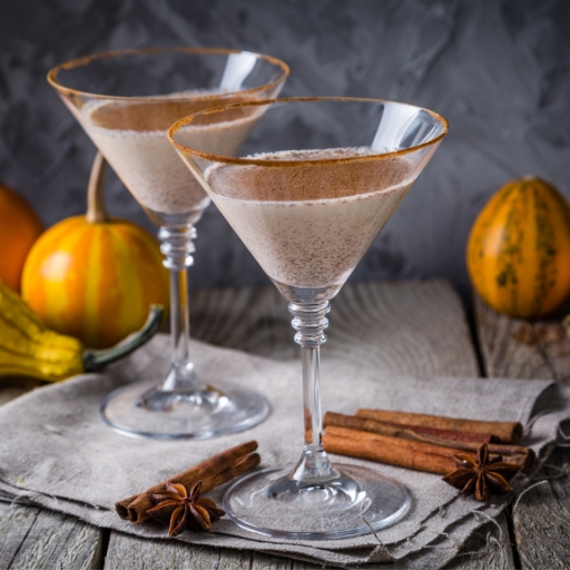 Dos vasos de un cóctel Autumn Martini, con ramas de canela y calabazas pequeñas a su alrededor.