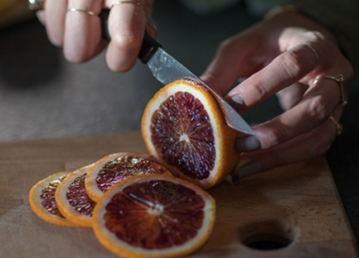 Una persona cortando una naranja sanguina en rodajas.