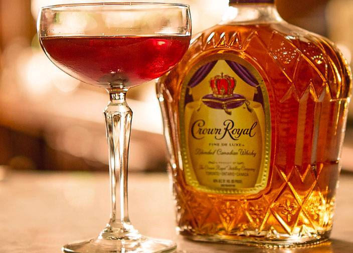 Eine Flasche Crown Royal Whisky auf einem Tisch neben einem Cocktail in einem Coupe Glas