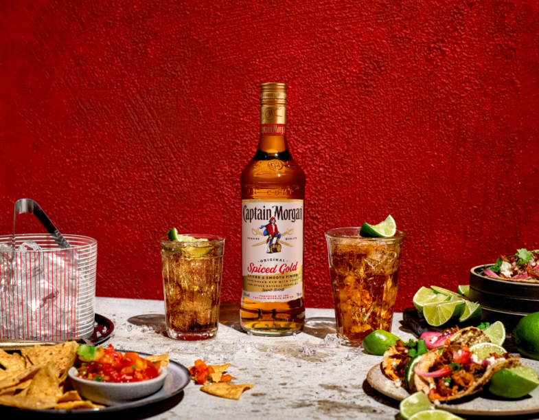 Bottle of Captain Morgan Spiced Gold rum on table beside plates of food against red background