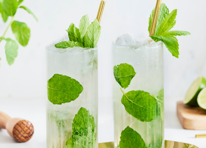  2 tall mojitos with nice mint leaves as decoration accompanied with gold straws  