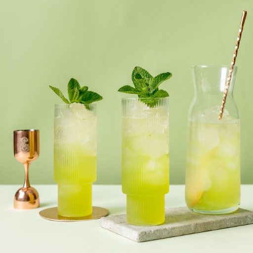 Image of two green cocktails on a table with a glass jug of the same cocktail