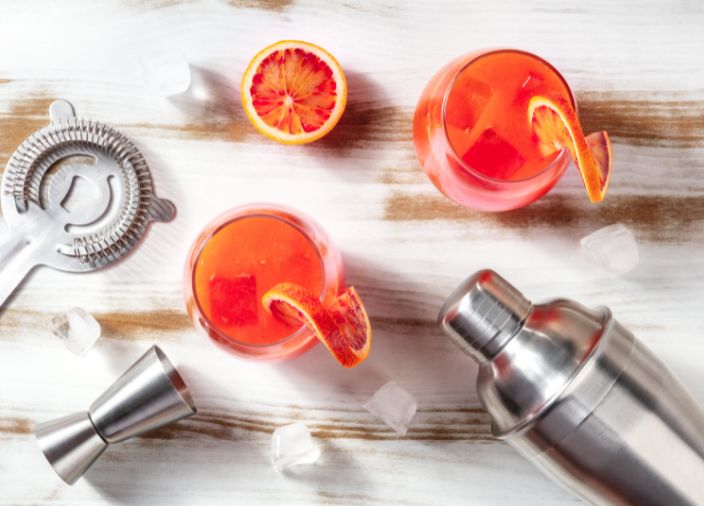 Dois coquetéis de gin de cor laranja com decoração de toranja, além de coqueteleira e coador