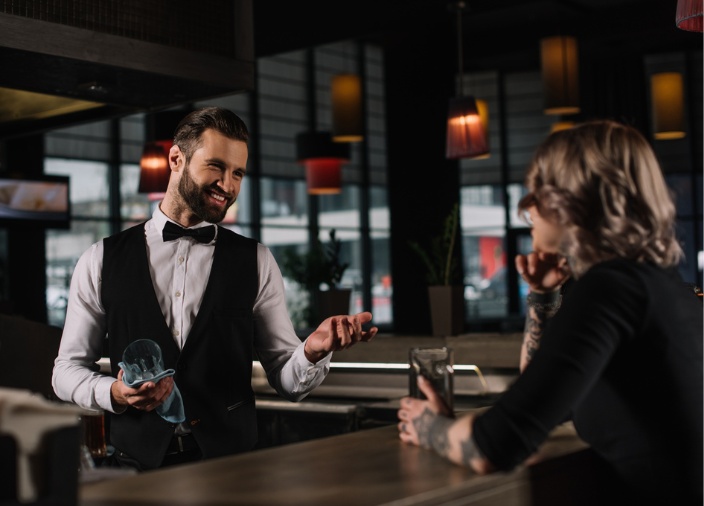 A male bartender smiling at a customer from across the bar.