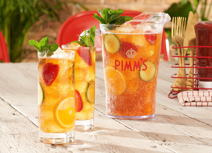 Jarra de cóctel Pimm's en una mesa junto a dos vasos altos llenos de líquido. 