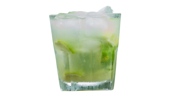 Copo baixo facetado e suado contendo um coquetel verde-claro e turvo. A bebida refrescante está repleta de cubos de gelo e pedaços de limão verde misturados no seu interior. Fundo branco isolado.