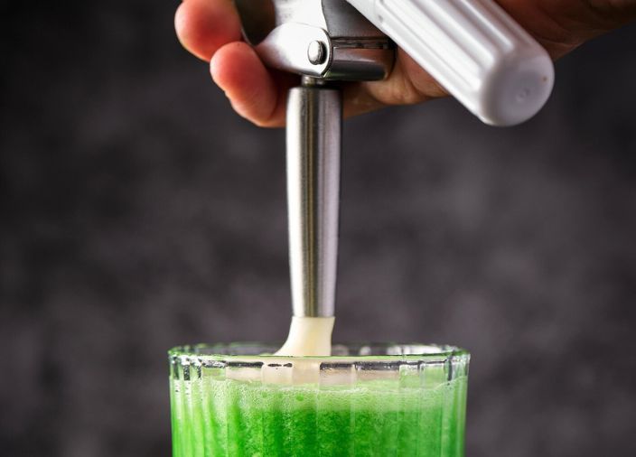 Cocktail foam being put on top of green cocktail