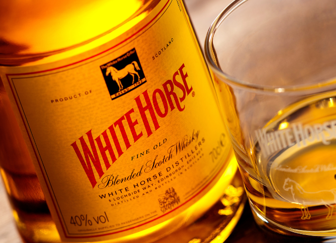 Eine Flasche White Horse Whisky auf einem Tisch neben einem Glas Whisky