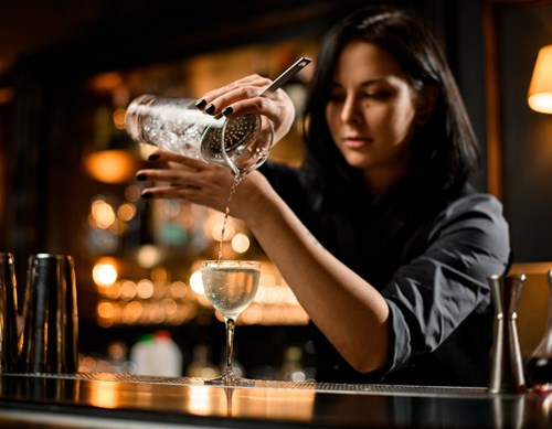 Barkeeperin schüttet Cocktail in ein Glas an der Bar