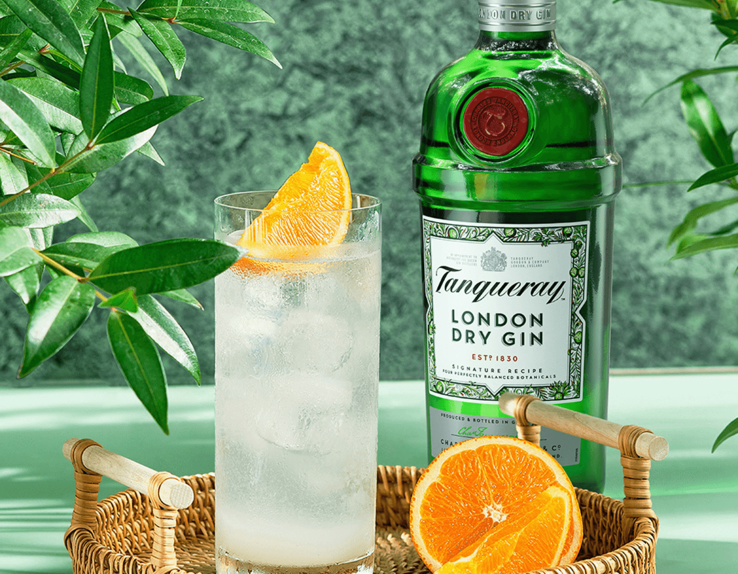 Eine Flasche Tanqueray London Dry Gin neben einem Cocktail und einer aufgeschnittenen Orange.