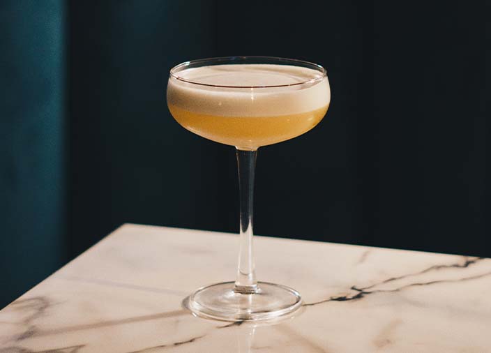 Cóctel amarillo en copa cupé con espuma blanca