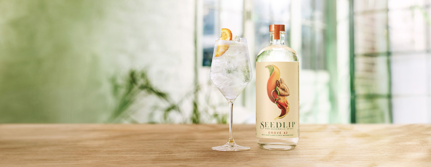 Eine Flasche Seedlip Grove 42 auf dem Tisch neben dem Cocktail
