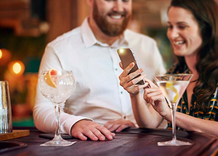 Zwei Menschen mit Cocktails schauen gemeinsam auf ein Smartphone