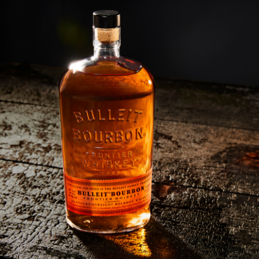 Botella de Bulleit Bourbon con un vaso adornado sobre una superficie de madera.