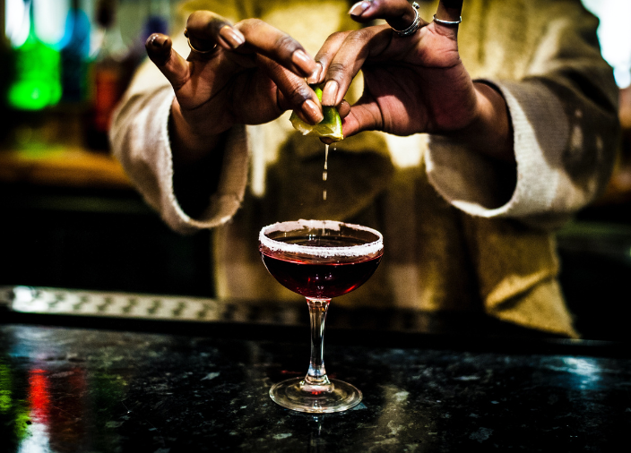 A bird shaped glass filled with a yellow cocktail drink and topped with a peacock feather.
