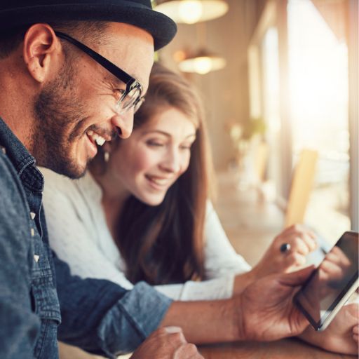 Man and Woman in bar looking and smiling at mobile phone to engage in social media 