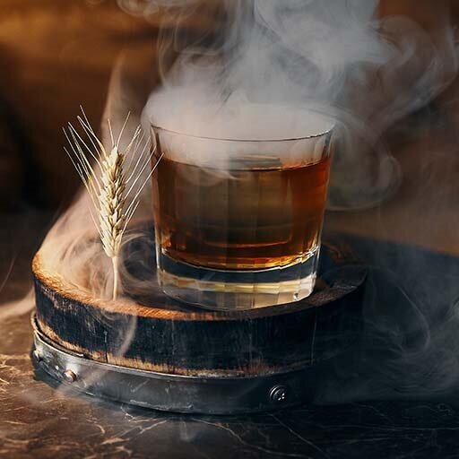 A clear tumbler glass filled with liquid surrounded by smoke.