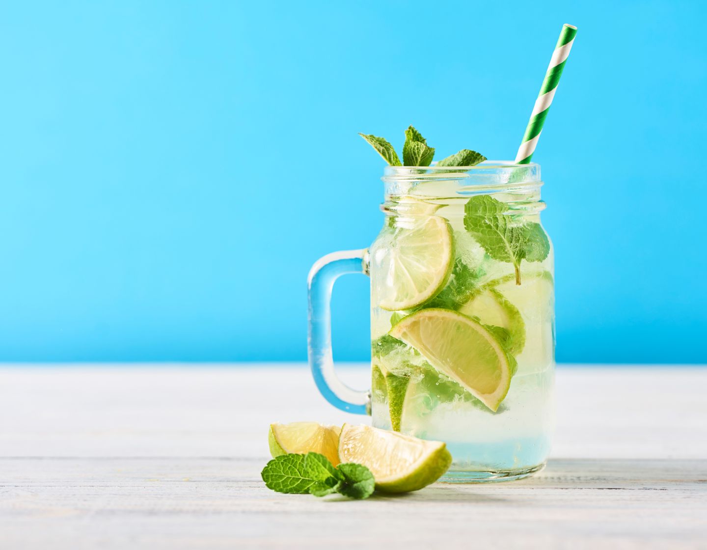 Un mojito servido con una pajita de papel verde y blanco sobre un fondo azul.
