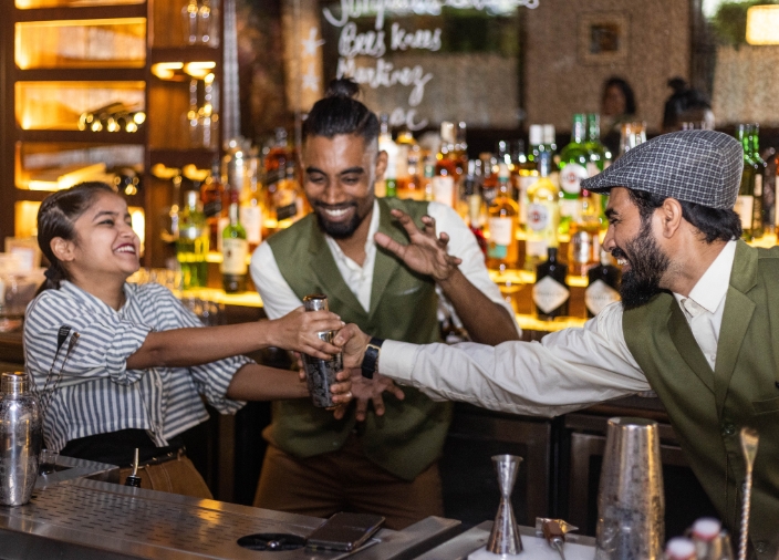 Three bartenders behind a bar jokingly fighting over a shaker.