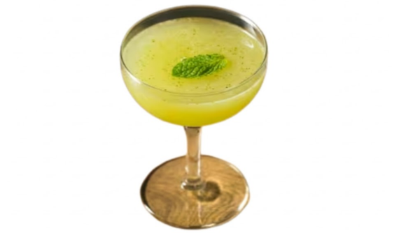 Taça coupe elegante contendo um coquetel opaco em tom verde-claro. A bebida é delicadamente decorada com uma única folha de hortelã fresca flutuando bem ao centro, cercada por minúsculos fragmentos verdes. Fundo branco isolado.