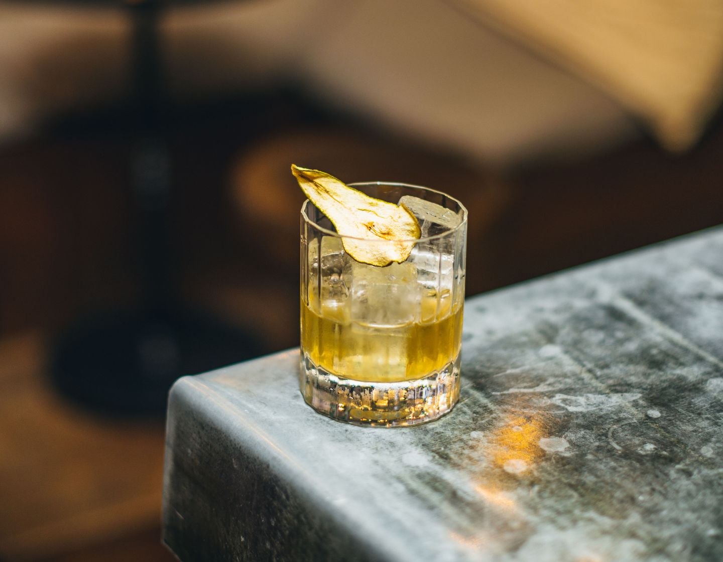 A Roe & Co whiskey serve with a dehydrated pear slice garnish on a table edge.  