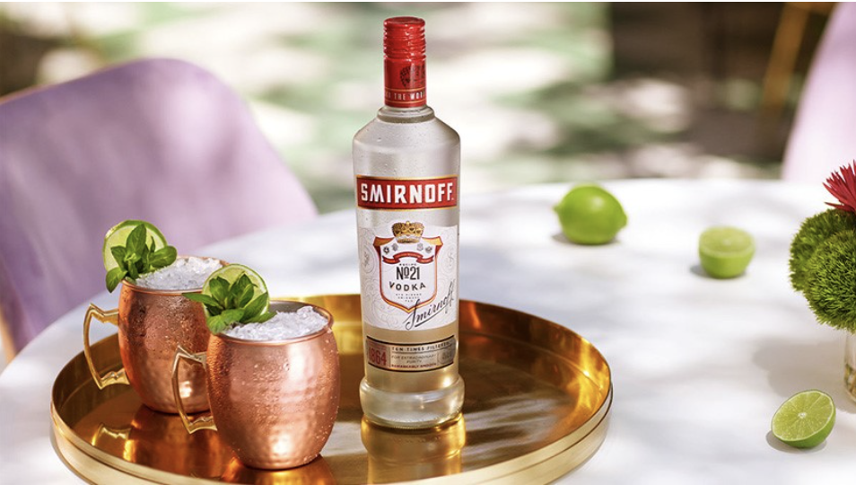 Flasche Smirnoff Wodka neben zwei Wodka-Getränken in Messingbechern.