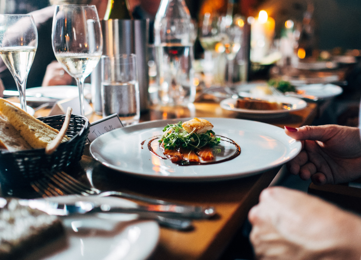Un cliente recibiendo un plato de comida, con un vaso de vino sobre la mesa