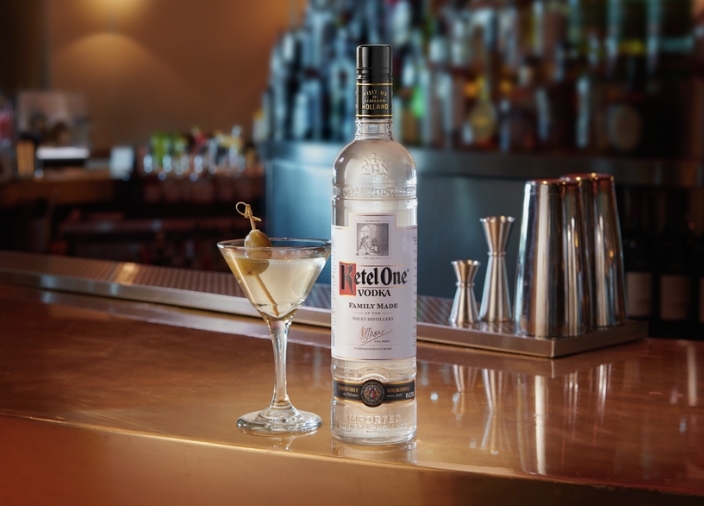 Bar counter with Ketel One Vodka bottle next to dirty martini with bartools in background