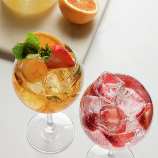 Dos coloridos cócteles en copas de ginebra con hielo y decoraciones de frutas.