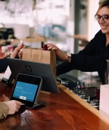 Un hombre y una mujer pagan en un bar utilizando un terminal de punto de venta con pantalla.