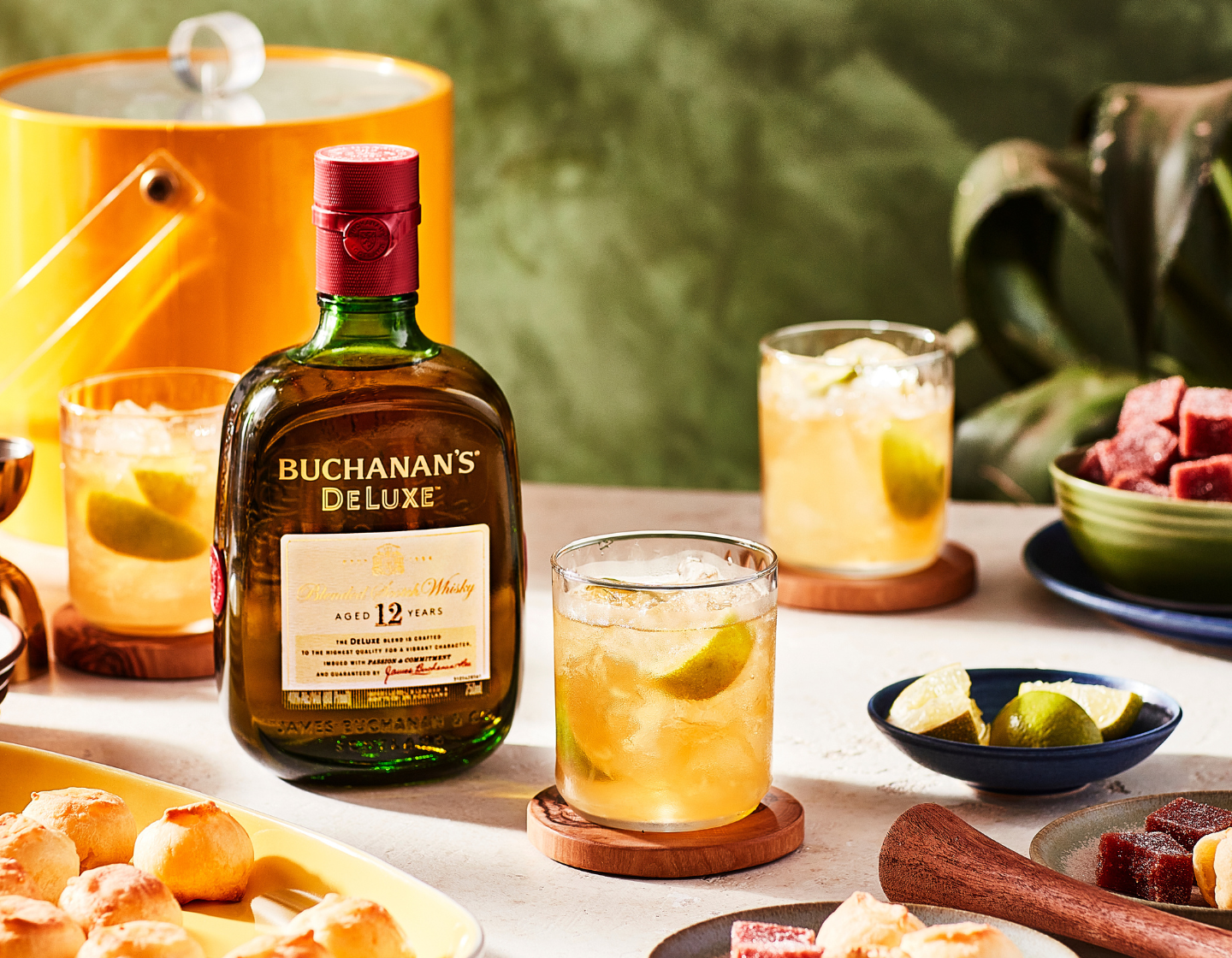 Botella de whisky Buchanan’s Deluxe sobre una mesa junto a diversos platos y bebidas