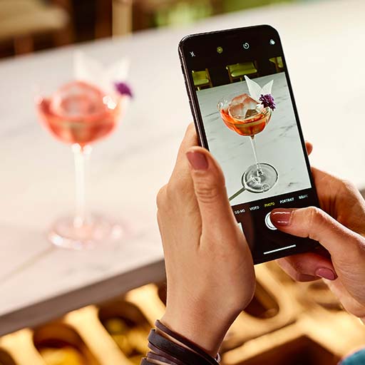 Um close de um bartender tirando uma foto de um coquetel com um smartphone.  