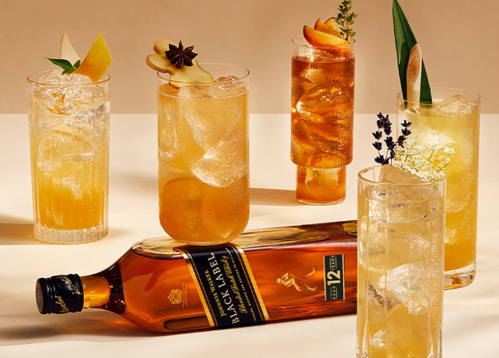 Johnnie Walker Black Lable bottle laying flat next to 5 different highball cocktails. 