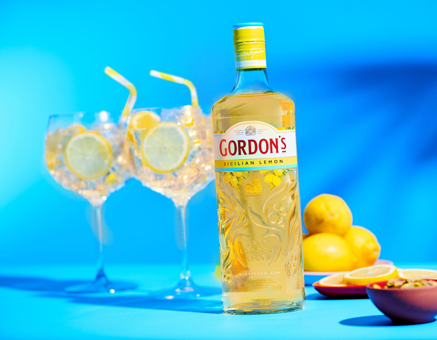 Garrafa de gin Gordon's Sicilian Lemon ao lado de dois copos de G&T em um fundo azul