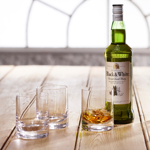 Una botella de Black & White en una mesa de madera rodeada por vasos de whisky