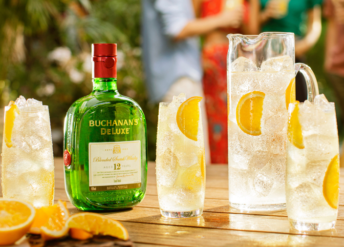 Botella de Buchanan’s Deluxe sobre una mesa rodeada de copas llenas de líquido